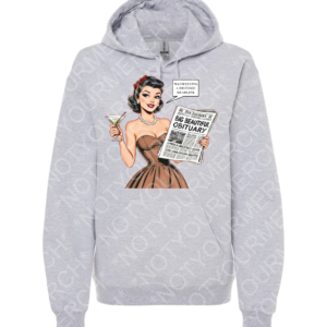 Unisex pullover hoodie featuring a retro-style illustrated woman holding a newspaper with the headline “Big Beautiful Obituary” and a speech bubble reading “Manifesting a Historic Headline.”