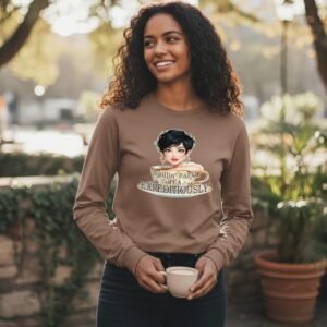 Woman wearing a long sleeve graphic shirt with an illustrated character and the phrase “Spillin’ Tea Expeditiously” while holding a cup.
